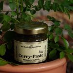 Curry, Currypaste indisch in einem Gläschen, welches vor einer Pflanze drapiert wurde